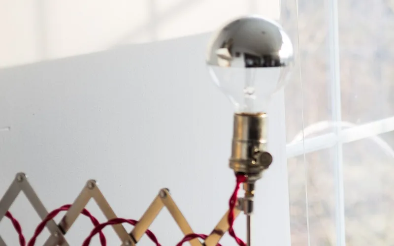 Scherenleuchte mit verspiegelter Glühlampe vor einem Sprossenfenster